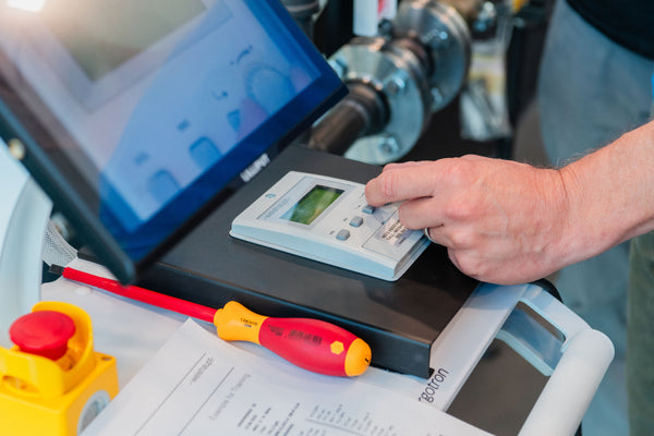 Person using a digital multimeter with a laptop and tools on a workbench