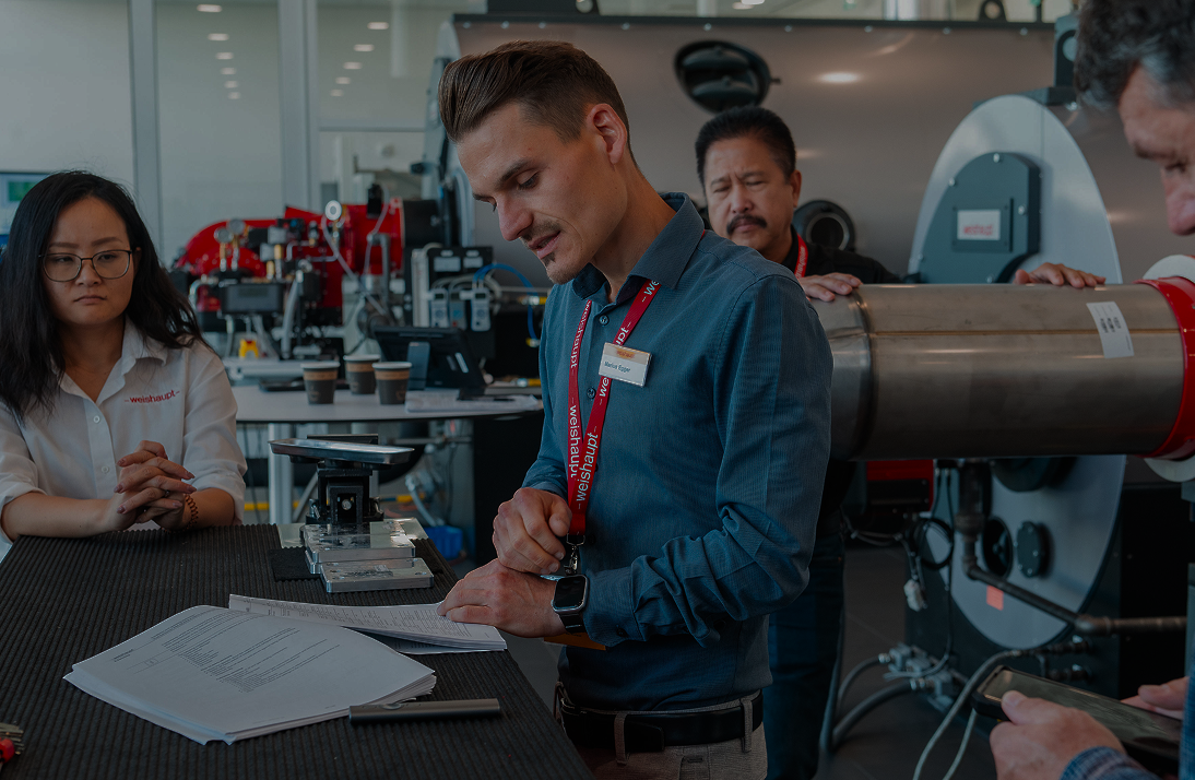 People in a workshop or lab setting with equipment and documents.