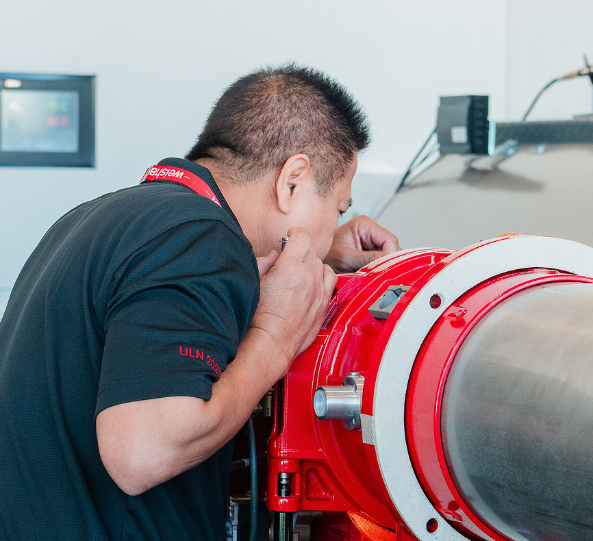 Person inspecting a large red and silver cylindrical machine.